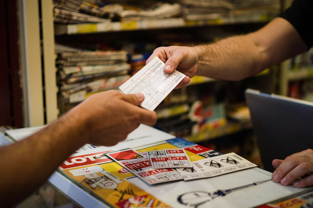 Hände an einem Kiosktresen, ein Lottoschein wird übergeben